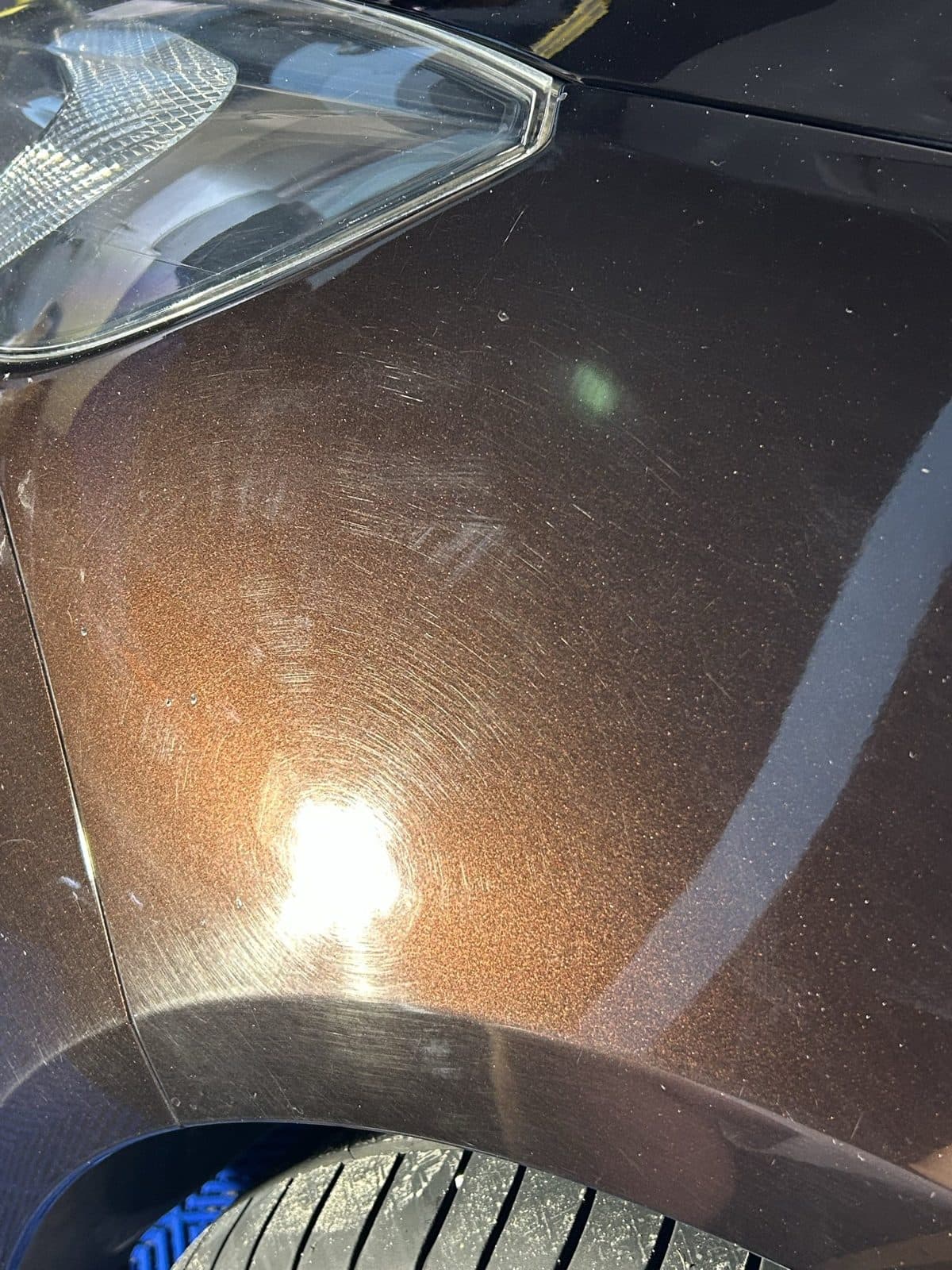 Pajęczyna rys i hologramów na brązowym lakierze w ostrym świetle